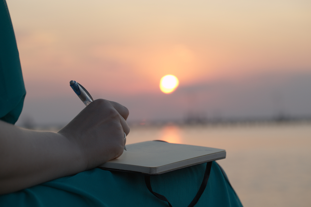 Close up view of womens hand writing with a sunset in the background.