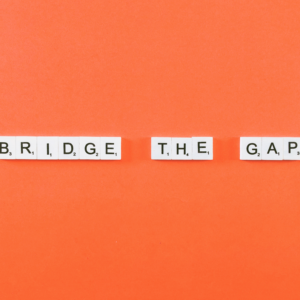 Scrabble tiles spell out BRIDGE THE GAP on a bright orange background