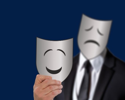 a person wearing a mask as a facade showing a sad face and holding another mask with a smiley face.